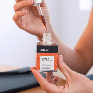 Woman holding bottle of broad-spectrum cbd and adaptogen tincture, with dropper full of oil