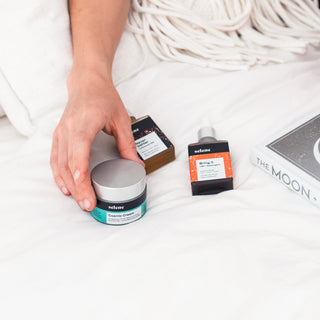 broad-spectrum CBD tincture, organic CBD and adaptogen tincture, and CBD botanical cream on bed, woman reaching for product