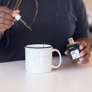 Woman dropping unflavored broad-spectrum CBD oil into tea mug