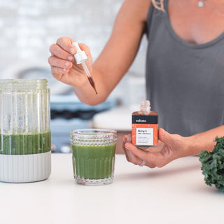 Woman dropping broad-spectrum cbd adaptogen tincture to green drink