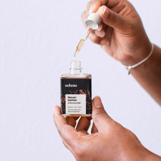 Woman holding bottle of CBD tincture, with dropper dripping oil