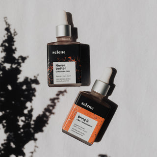 Never Better CBD tincture bottle and Bring It CBD and adaptogen tinctures bottles, laying next to plant shadows
