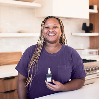 Woman smiling and holding bottle of Never Better broad spectrum CBD oil