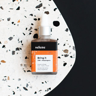 Bottle of Bring It CBD and adaptogen tincture on speckled surface
