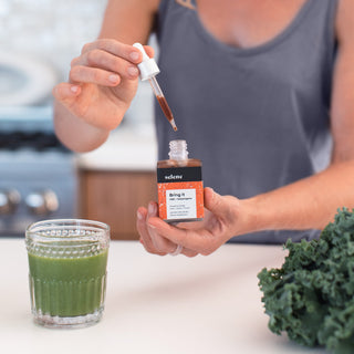 Woman using CBD and adaptogen tincture in green juice