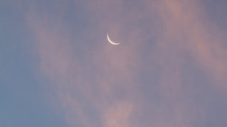 crescent moon at dusk, behind pink clouds