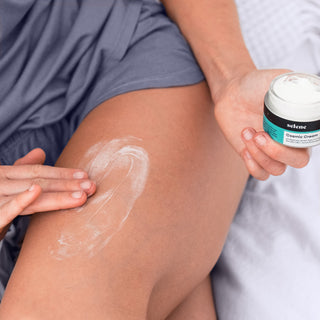 Woman applying organic CBD botanical cream to thigh, soothes muscle and joint pain